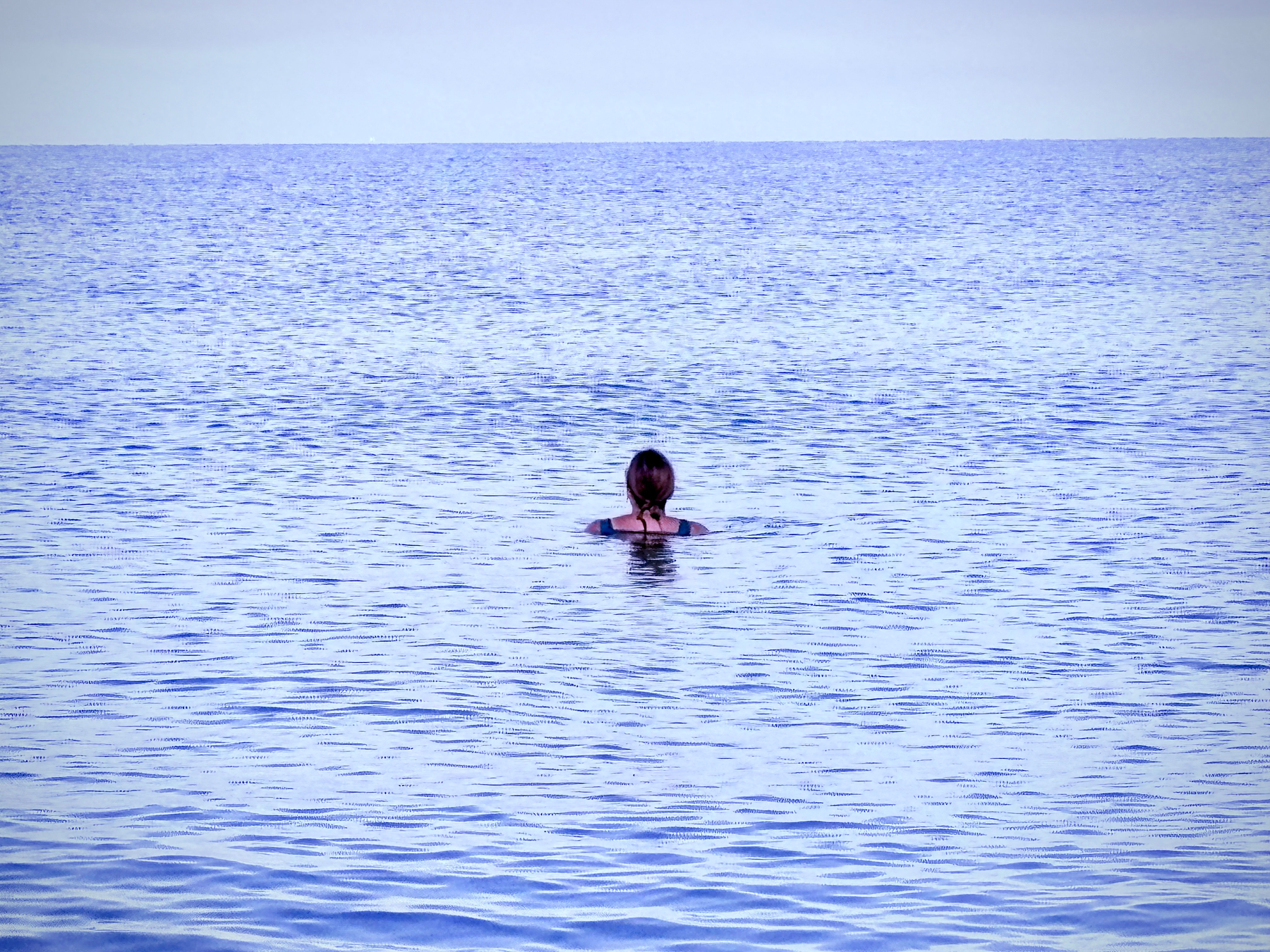 A person is seen swimming alone in a vast expanse of calm blue water.
